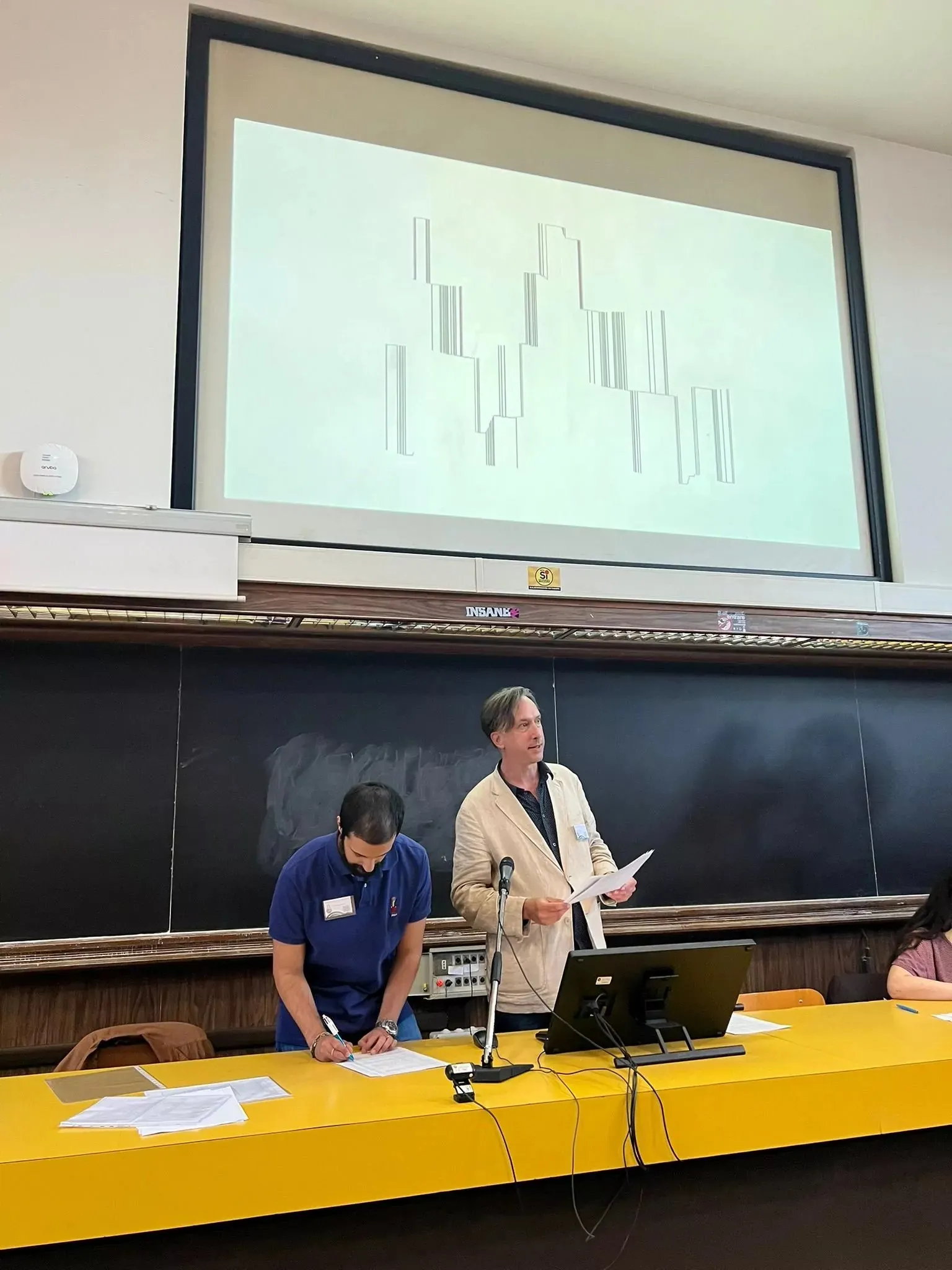 Alex May speaking at Sapienza University of Rome beneath a projected image during the Economies and [Microbial] Ecosystems event.