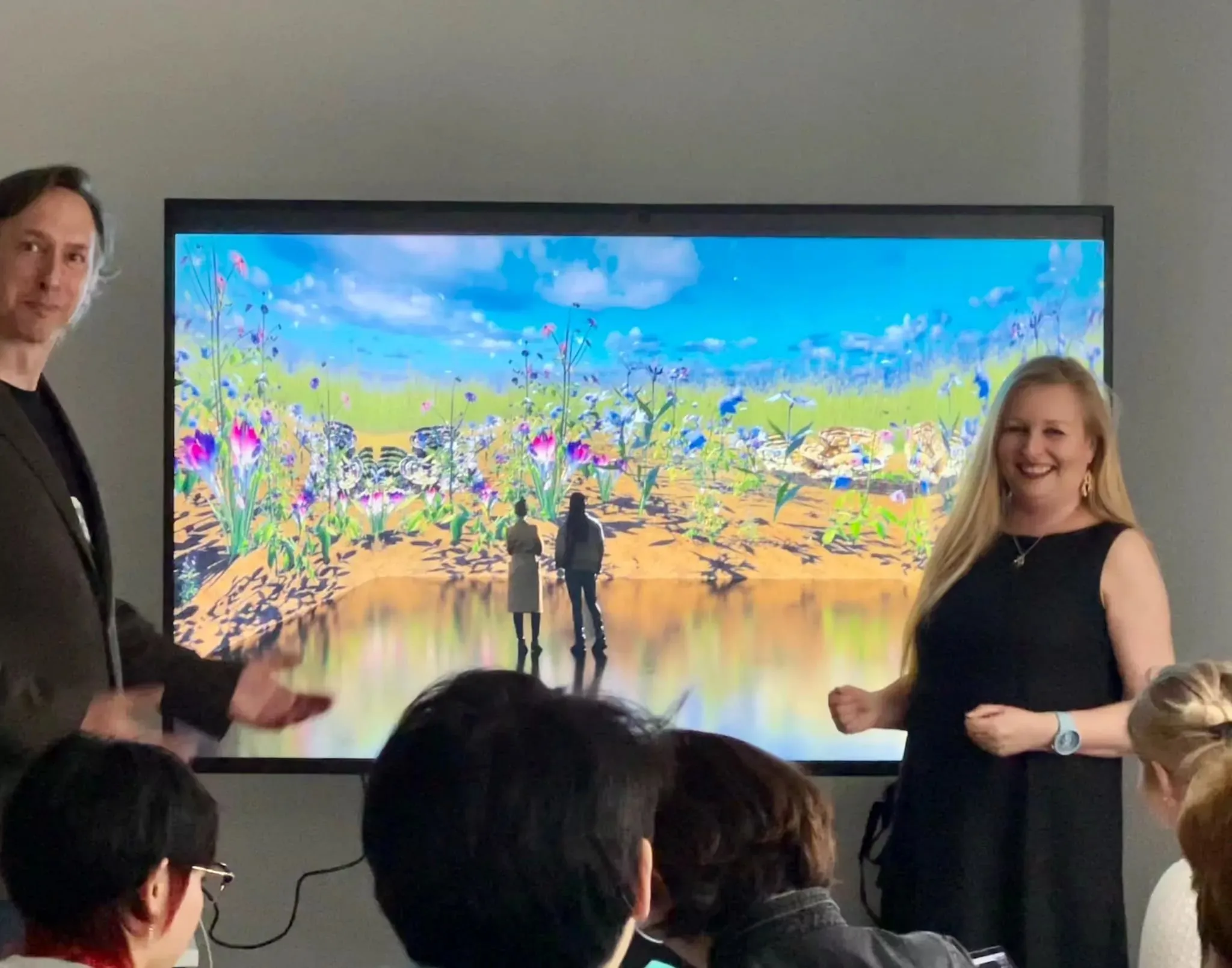 Alex May and Anna Dumitriu speaking in front of a large screen showing Physic-AI Garden at the Royal College of Art