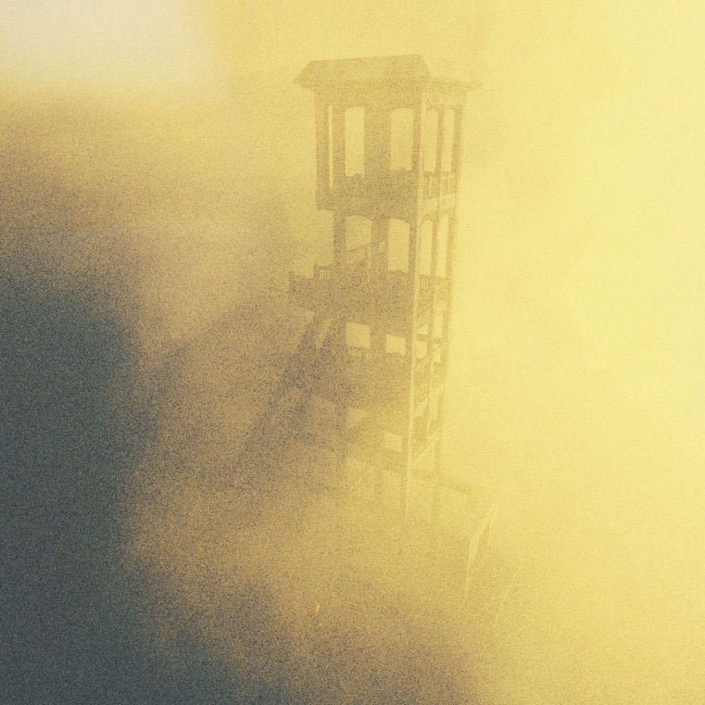 The form of a large industrial coal mining tower is just visible through a thick cloud of smoke